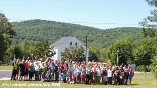 community standing and waving in front of white town hall  